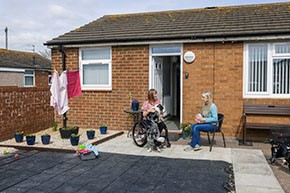 Two women in a back garden, one sitting in a wheelchair the other on a seat